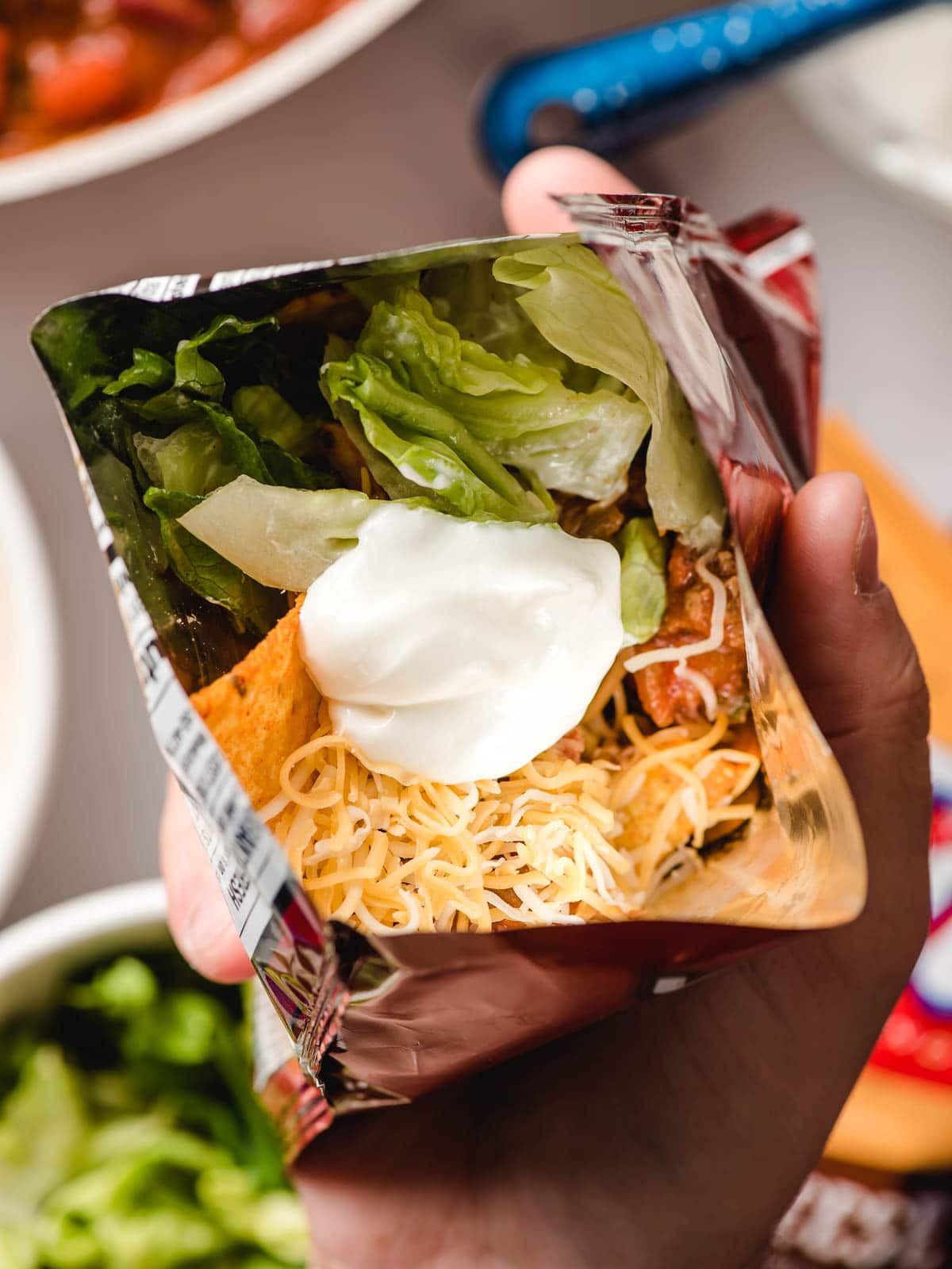 Open bag of chips layered with taco meat, lettuce, sour cream, and cheese.