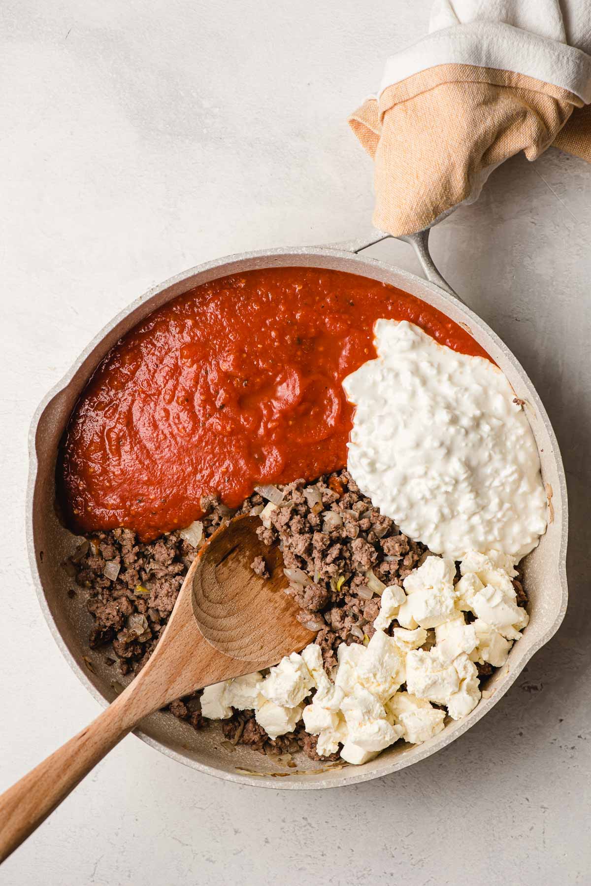 Skillet with sauteed ground beef mixture, tomato sauce, cottage cheese, and cubed cream cheese.