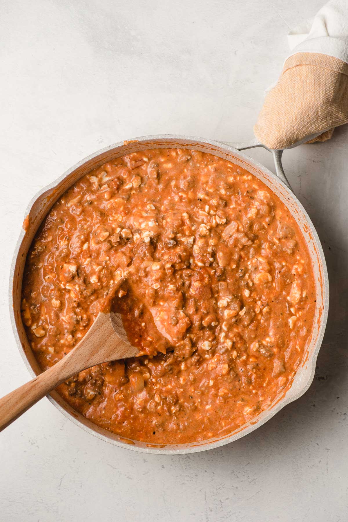 Skillet with a creamy tomato-y ground beef sauce being stirred by a wooden spoon.