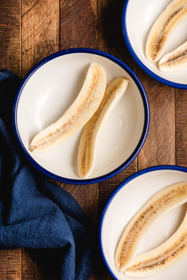 Three blue-rimmed bowls, each with a halved banana in them.