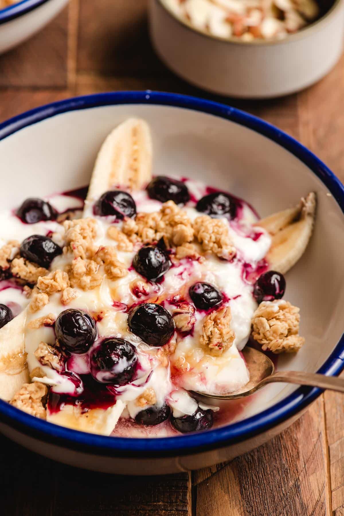 Blue-rimmed bowl with a split banana, yogurt, blueberries, granola, and honey.