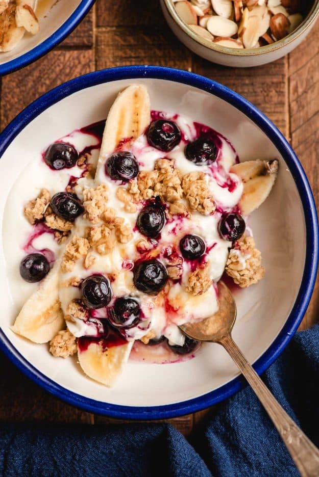 Breakfast banana split in a white bowl, topped with blueberries, granola, and honey.