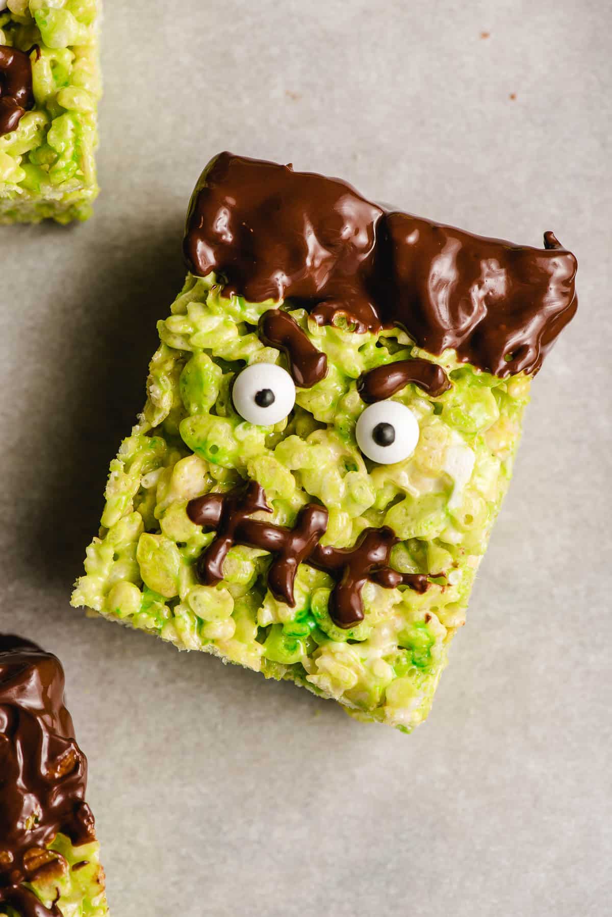 Frankenstein rice krispie treat with angry eyebrows, googly eyes, and a chocolate stitched mouth.