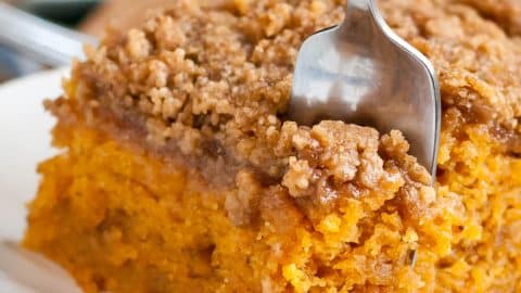 Fork taking a bite out of a slice of pumpkin crumb cake on a plate.