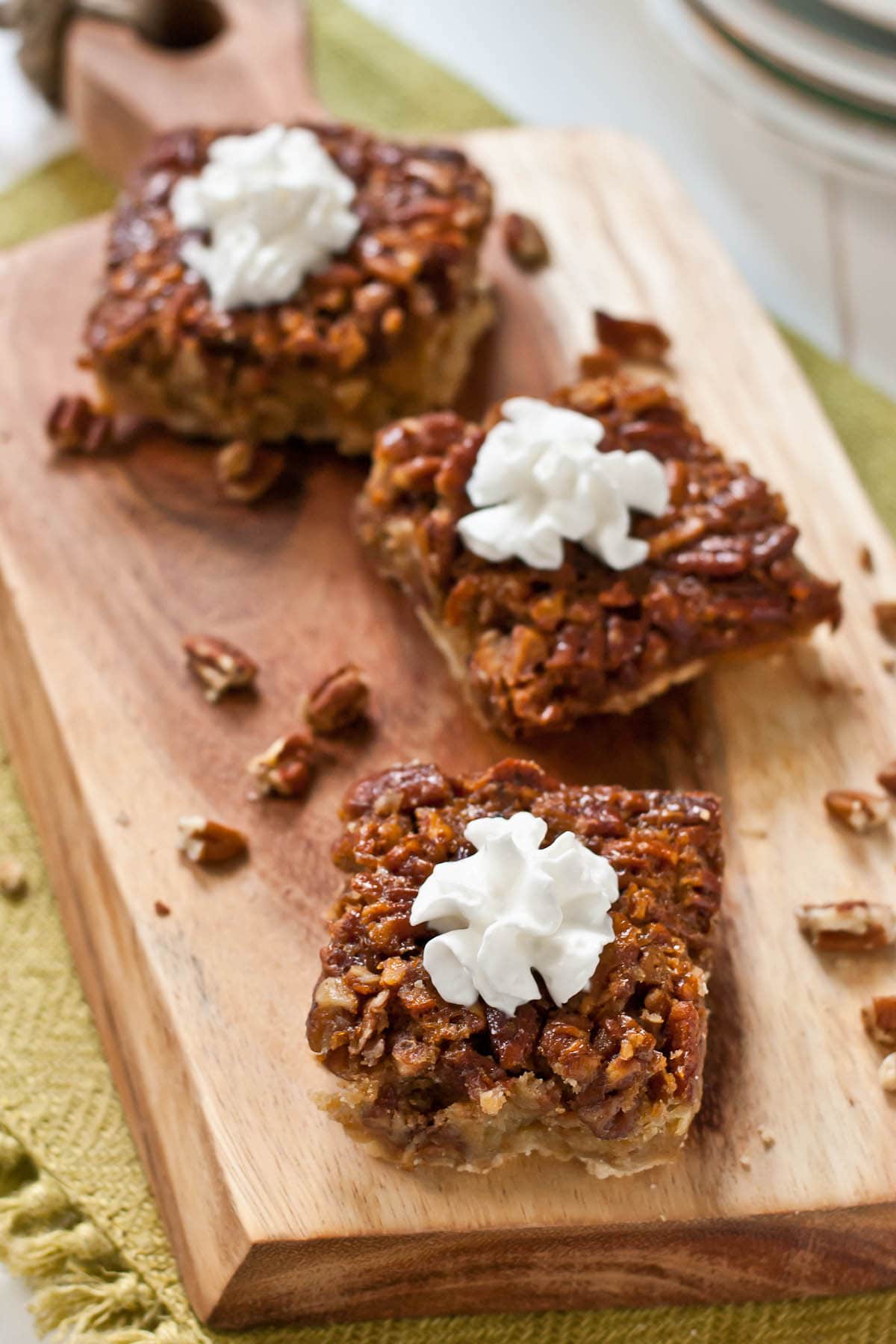 three pecan pie bars topped with whipped cream served on a board