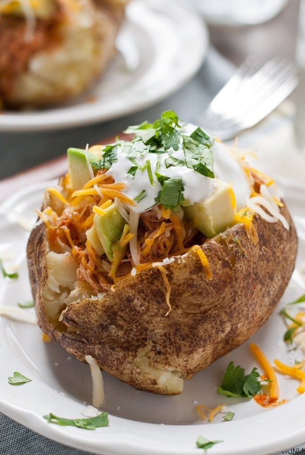 These Chicken Enchilada Baked Potatoes are loaded with saucy shredded chicken, cheese, sour cream, and avocado! A perfect weeknight meal.