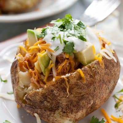 A baked potato loaded with shredded chicken, avocado, sour cream, and cilantro.
