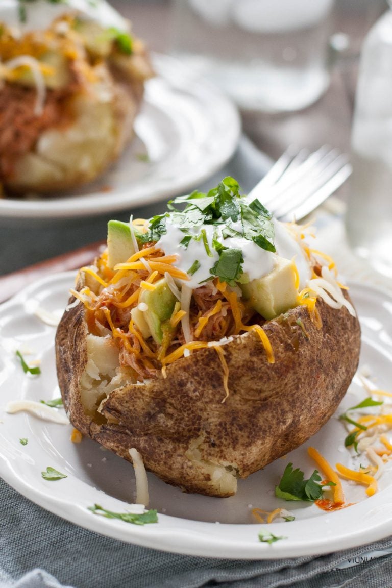 Loaded baked potato with shredded cheese, enchilada chicken, avocado, sour cream, and cilantro.