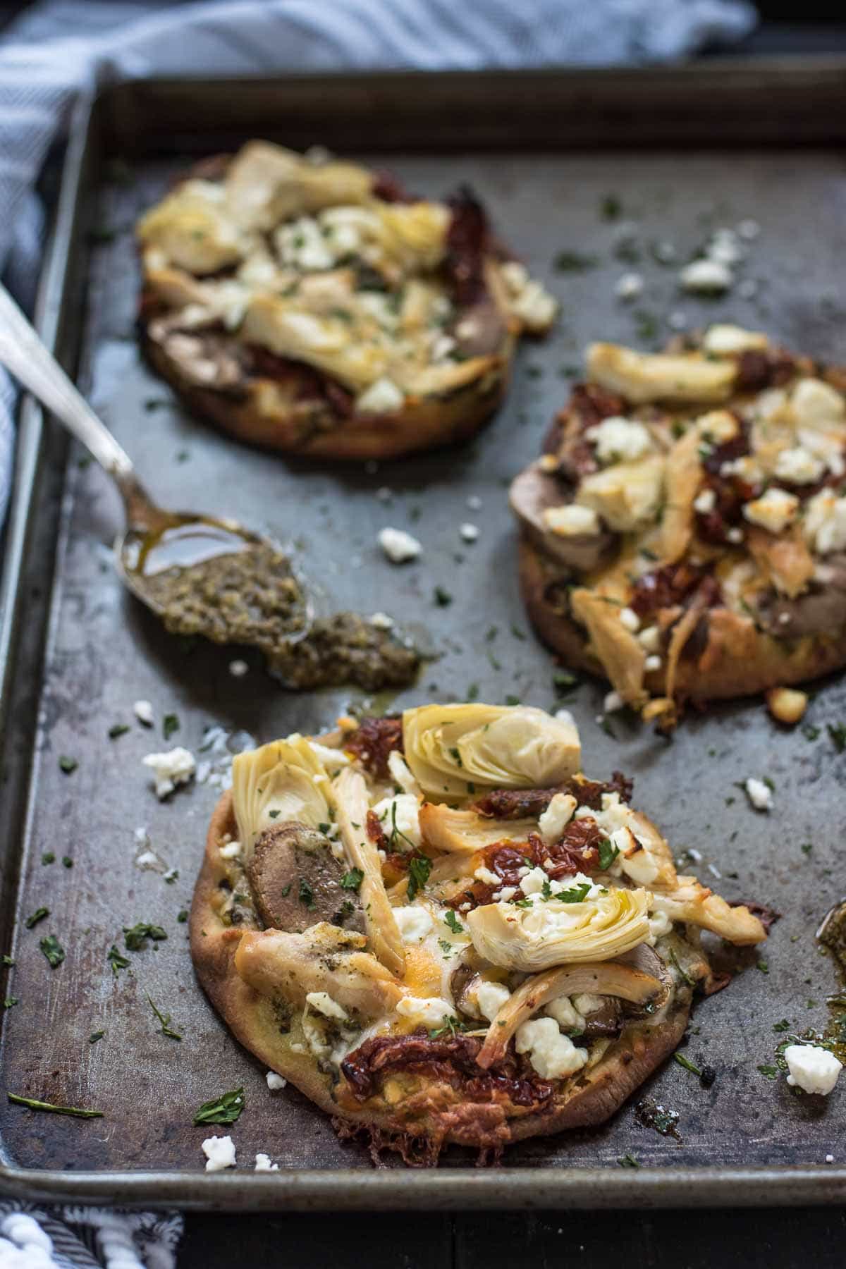 These mini pizzas loaded with feta, chicken, sundried tomatoes, and artichoke make a quick and easy weeknight meal.
