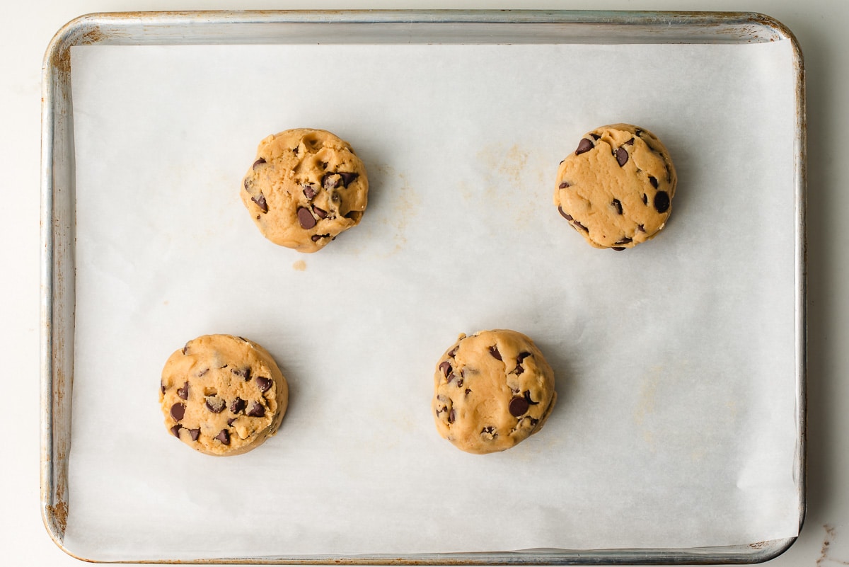 4 large balls of cookie dough on a baking sheet.
