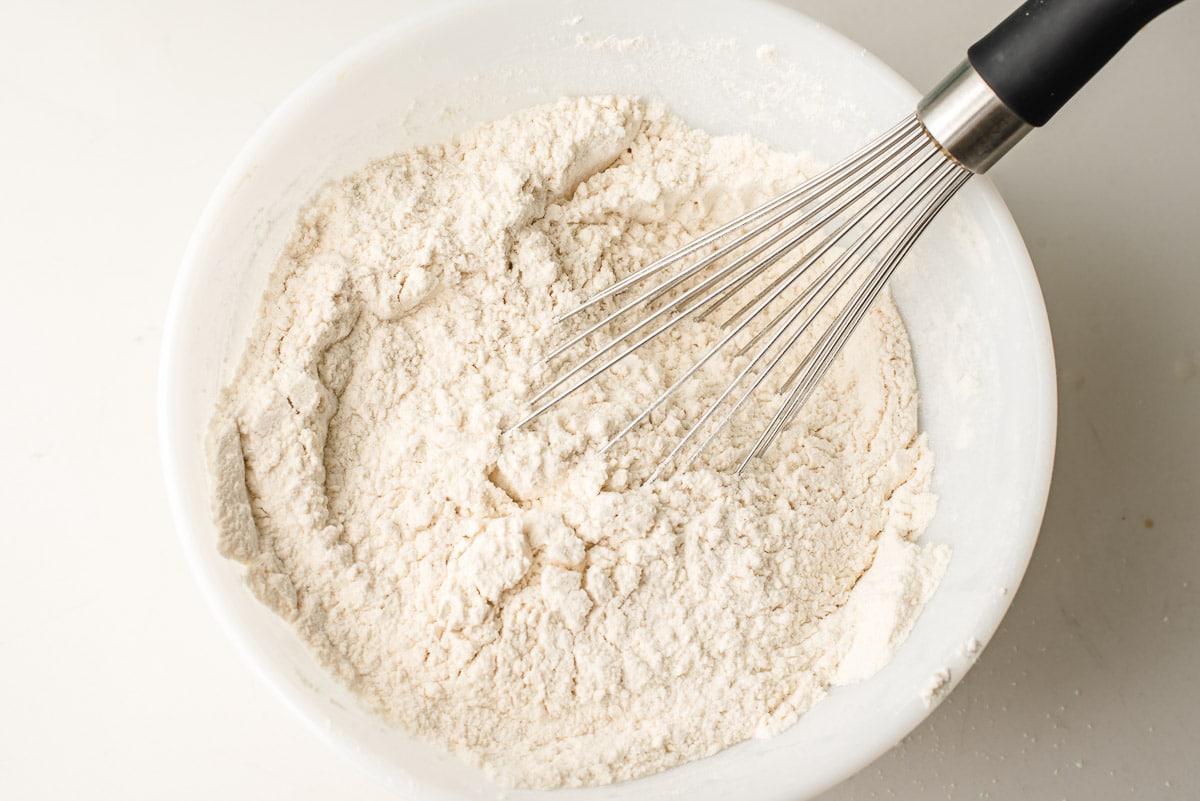 Flour, cornstarch, salt, baking soda and baking powder whisked together in a white bowl.
