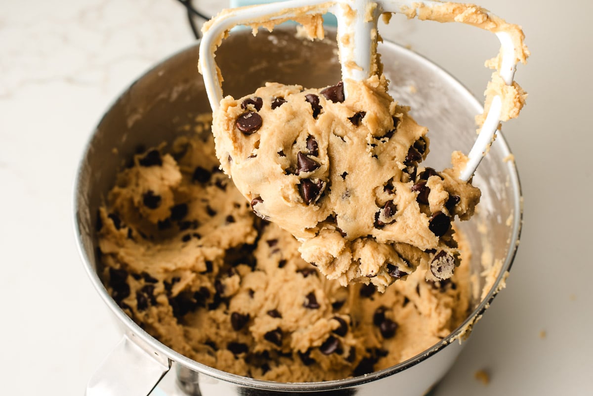 Chocolate chunk cookie dough on the beater of an electric mixer.