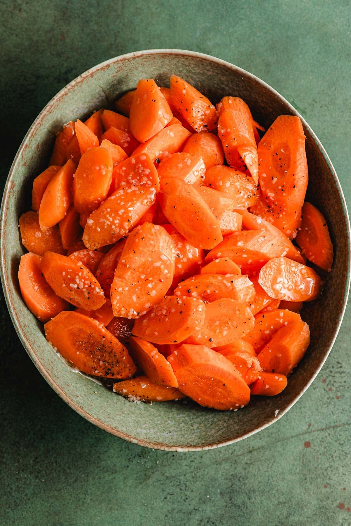 Sliced carrots tossed with honey, olive oil, salt and pepper in a green bowl.