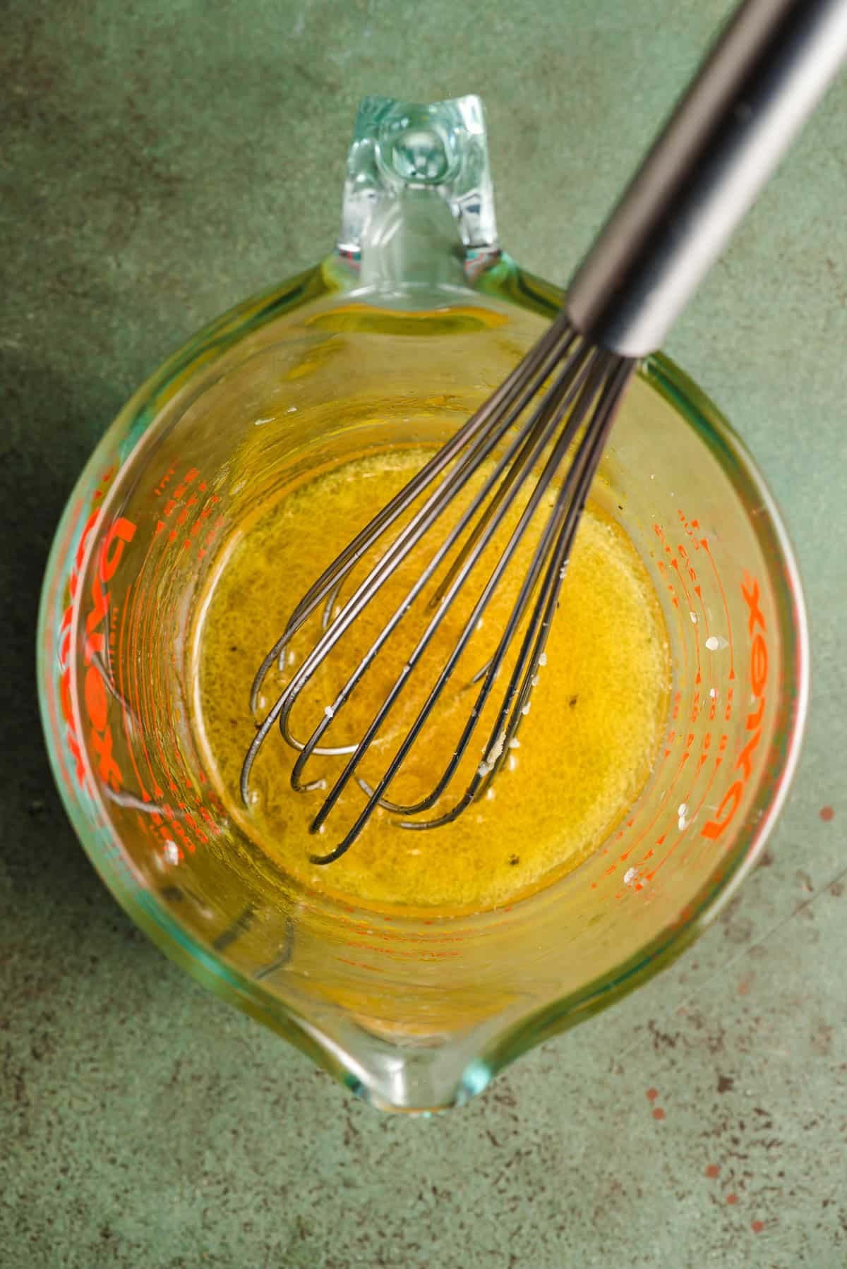 Honey, cider vinegar, lemon juice, and olive oil whisked together in a measuring cup.