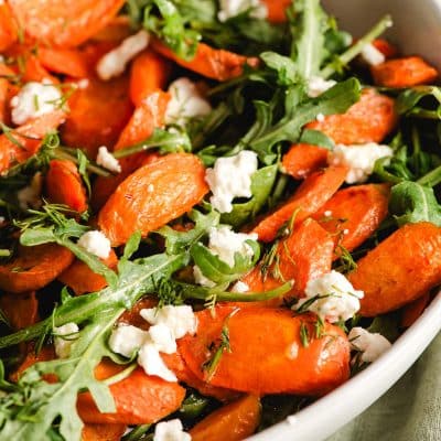 Roasted carrot salad with arugula and feta cheese in a white bowl.