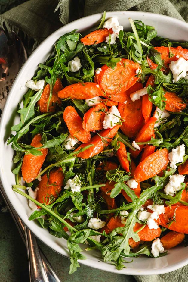 White bowl filled with arugula, roasted carrots, and feta.