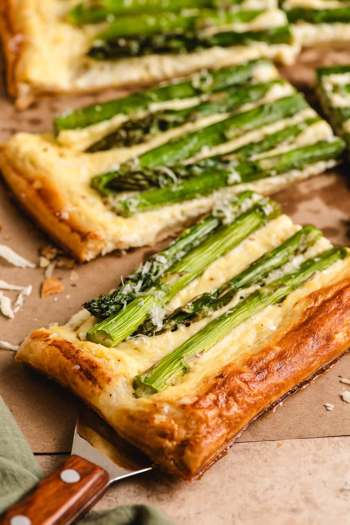 Slice of parmesan asparagus tart with a spatula underneath.
