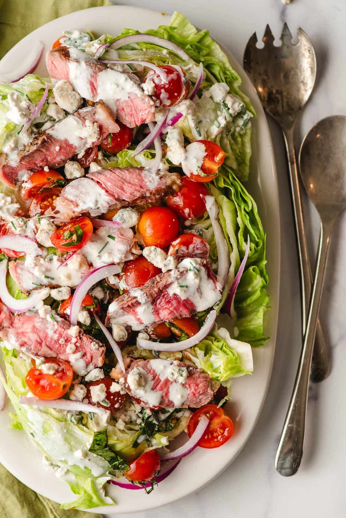 Iceberg wedge salad with steak, blue cheese dressing, tomatoes, and red onion.
