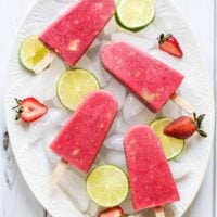 Berry Avocado Popsicles on a large white platter with ice cubes, lime slices, and strawberries.