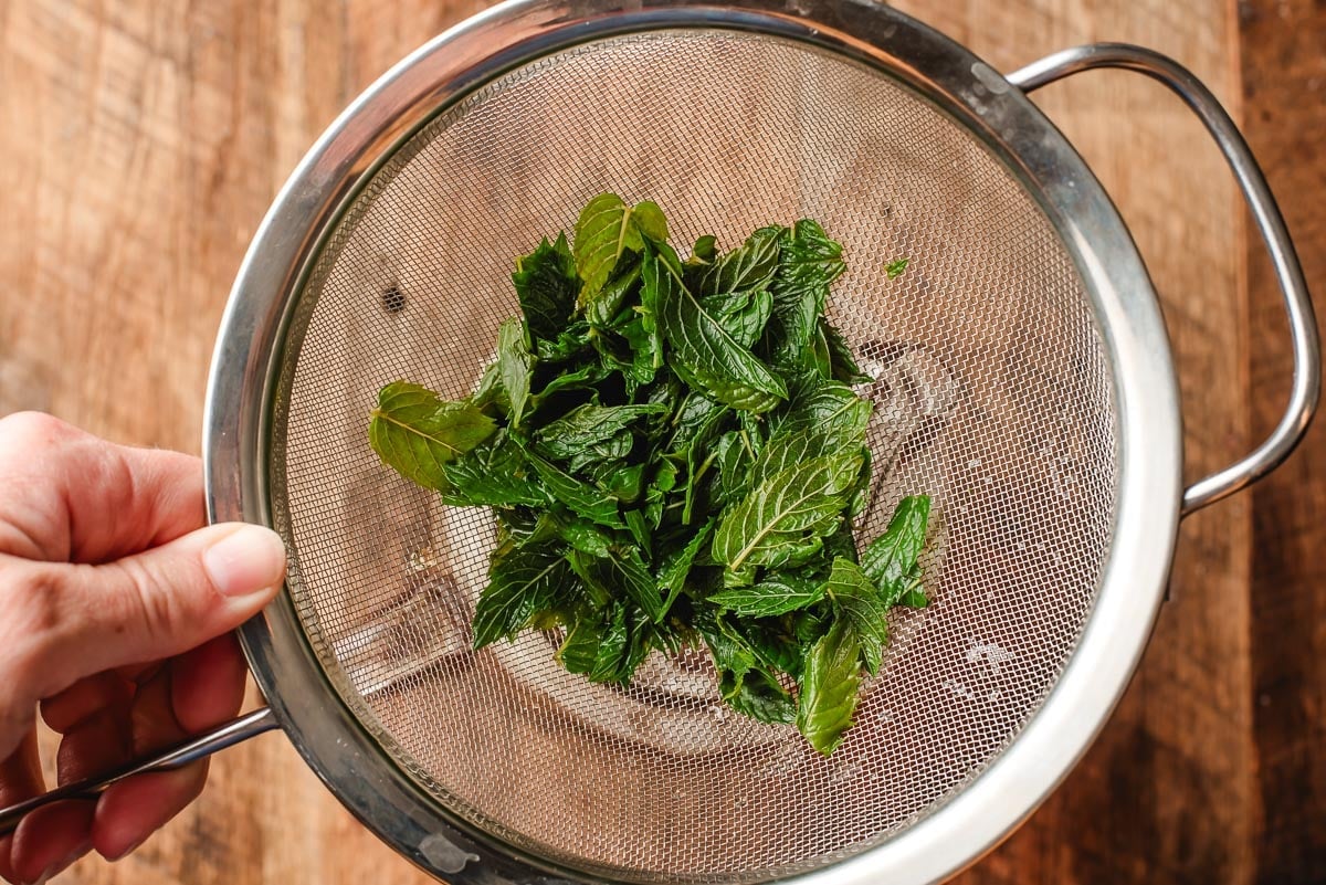 Spearmint leaves caught in a fine mesh strainer.