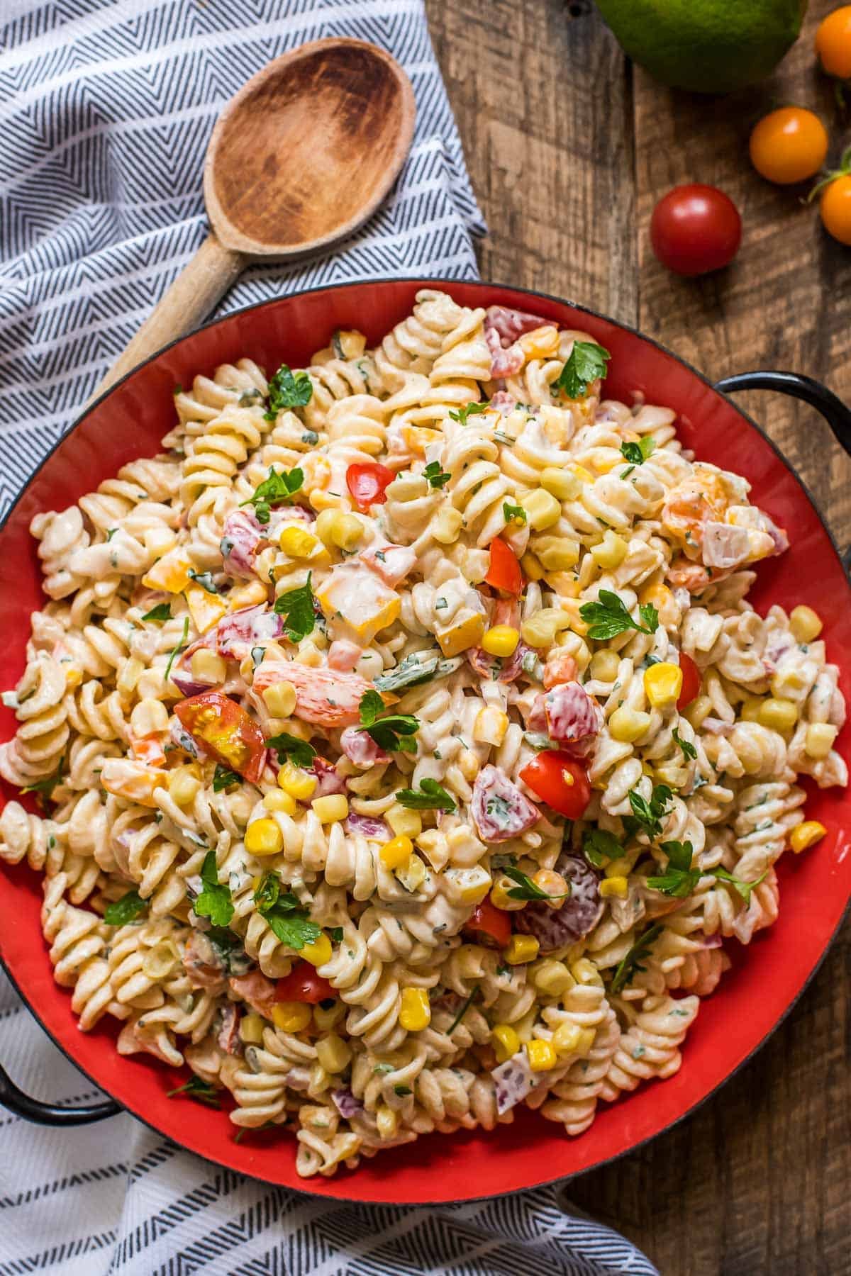 Southwestern pasta salad in a large red serving bowl with a wooden spoon.