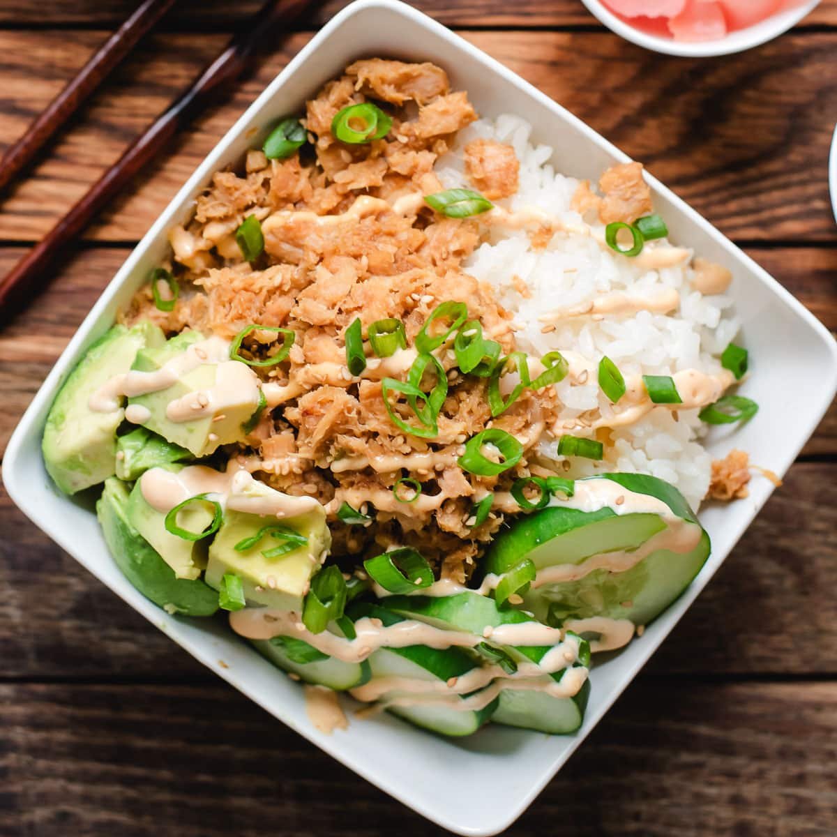 Tuna sushi bowls with spicy mayo, avocado, and cucumber in a square bowl.