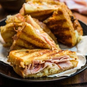 Gruyere grilled cheese sliced in half to reveal the melty cheese, ham slices, and caramelized onions.