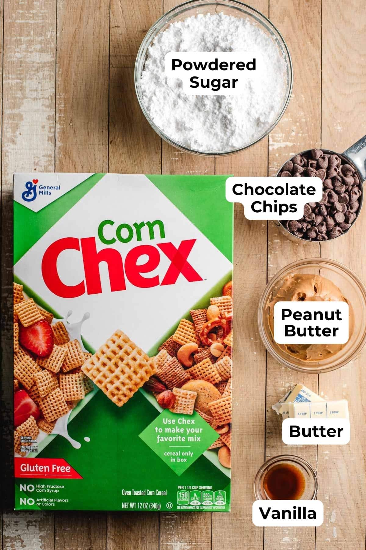Box of corn chex, powdered sugar, chocolate chips, peanut butter, butter and vanilla extract on a wooden background.