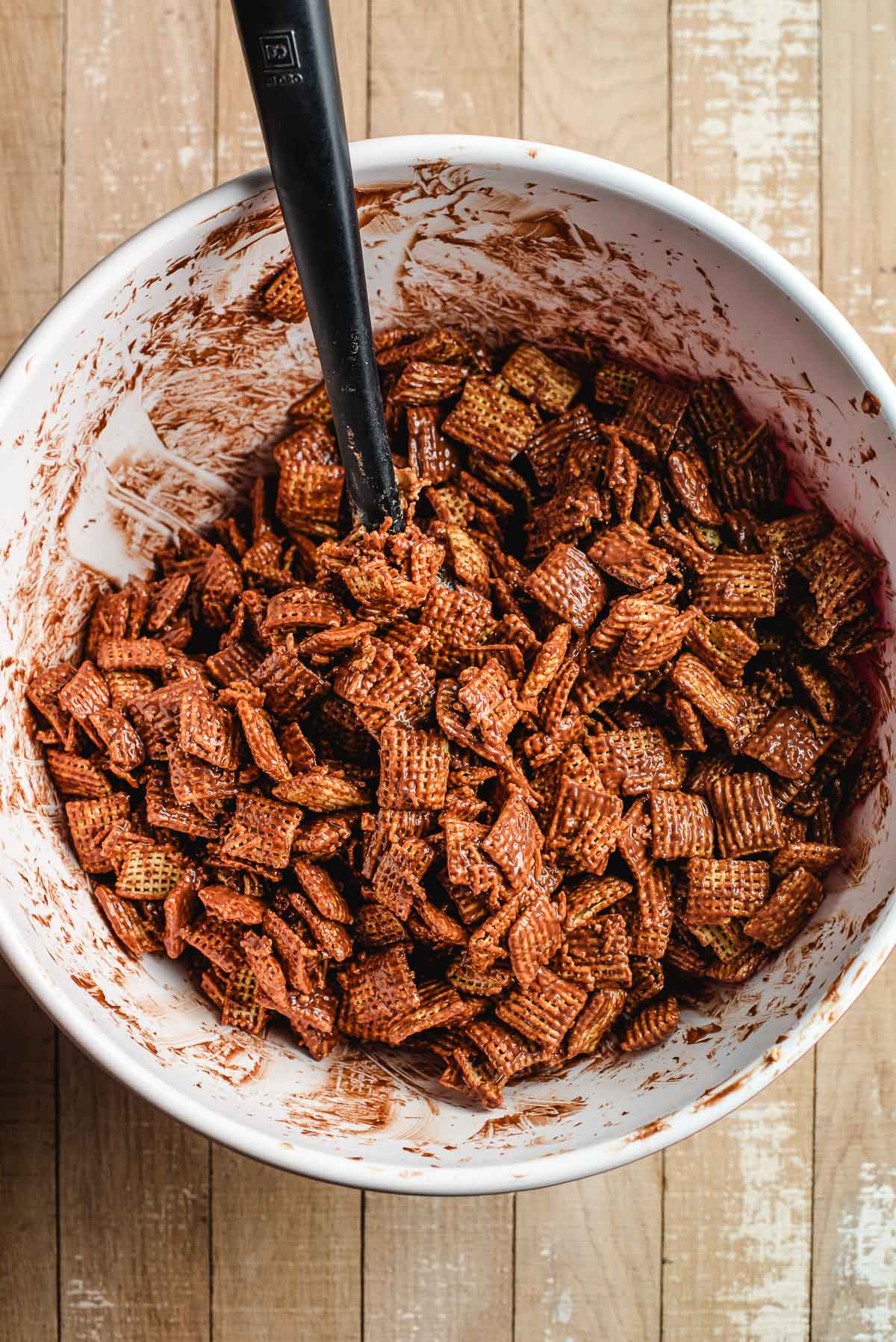 Melted chocolate and peanut butter mixed over Chex cereal in a large white bowl.