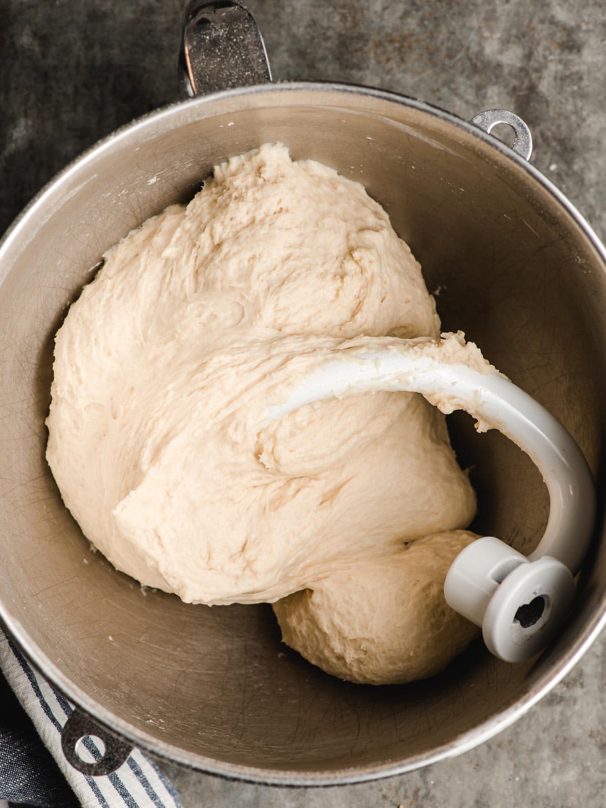 Dough hook in the bowl of an electric mixer with white bread dough.