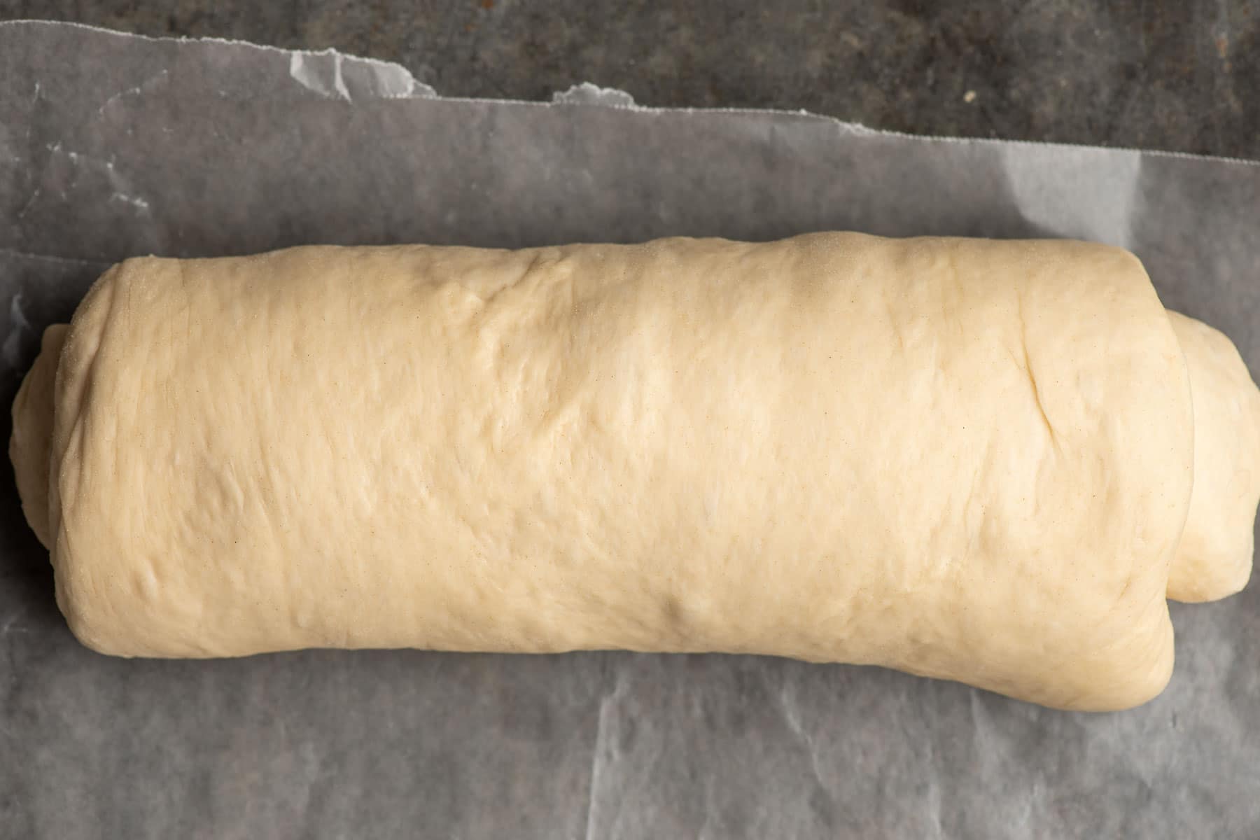 Bread dough rolled up on a piece of parchment paper.