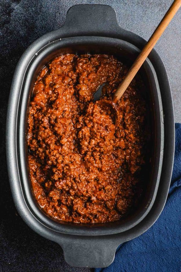 Sloppy joes in a crock pot being scooped with a wooden spoon.