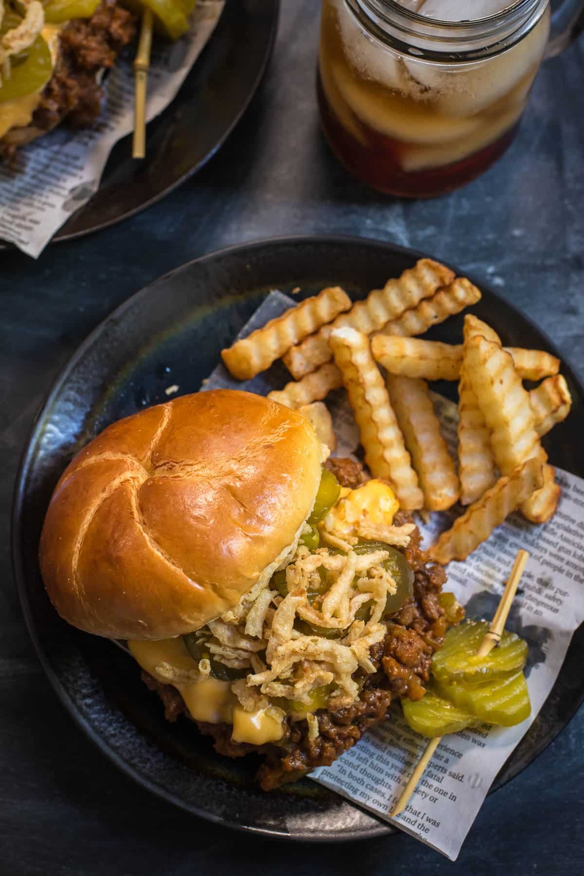Plate with a homemade sloppy joe sandwich, crinkle cut fries, and pickles speared on a toothpick.