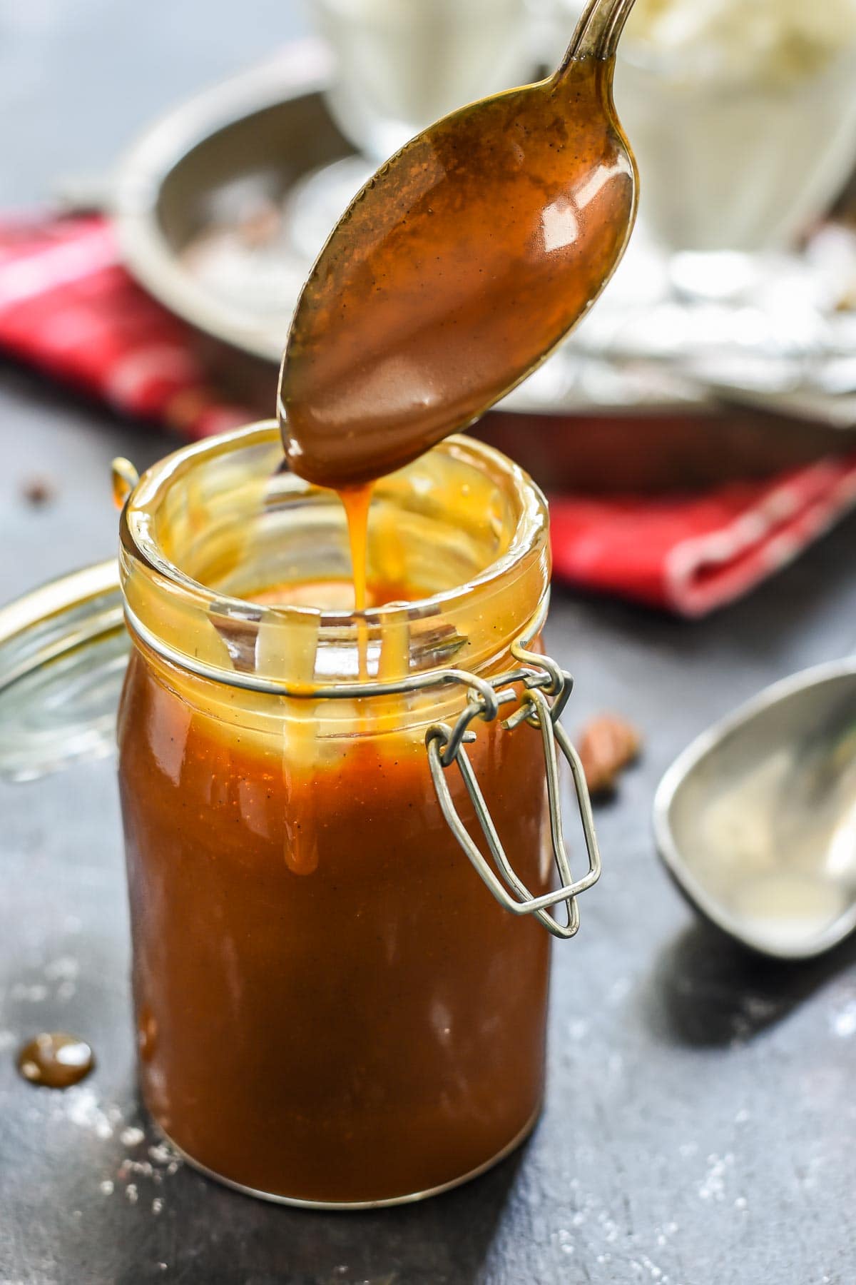 a spoon drizzles homemade caramel sauce from a jar