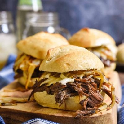 Pot roast sliders on a cutting board with a blue gray background.