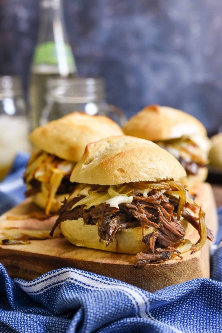 Pot roast sliders on a cutting board with a blue gray background.