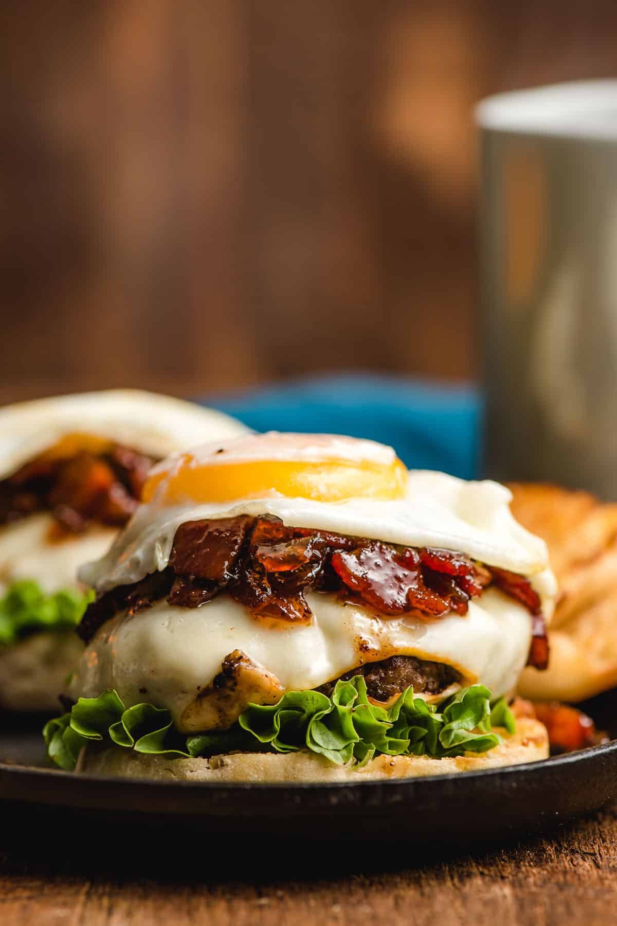 English muffin topped with lettuce, cheeseburger, bacon jam, and a fried egg.