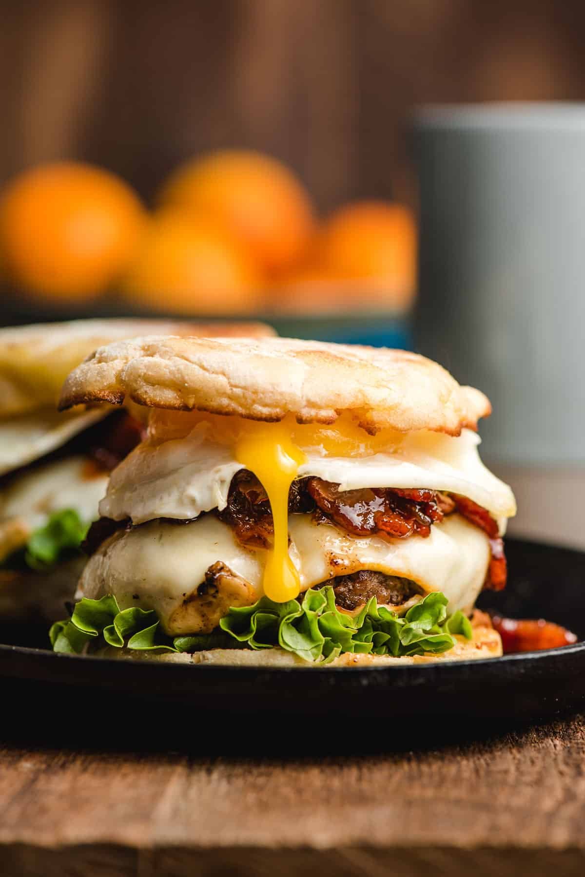 Breakfast burger featuring an English muffin, cheeseburger, salary jam, and a fried egg with the yolk spilling out the side.