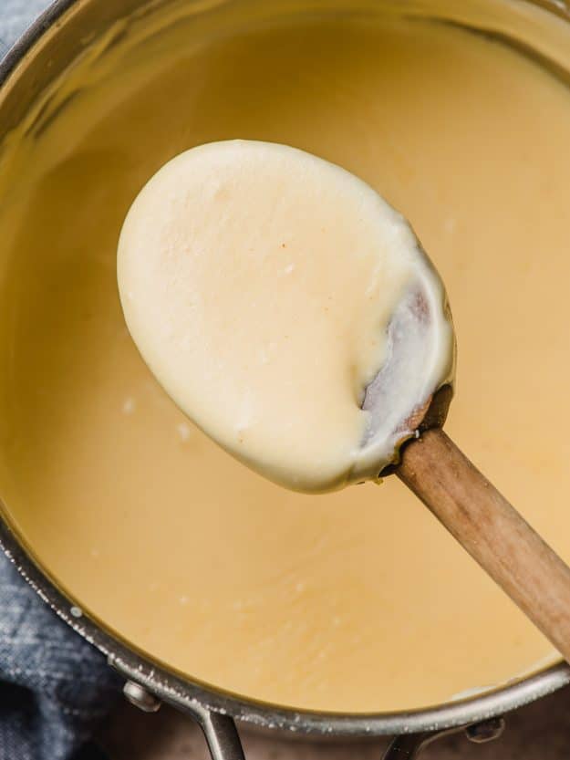 Wooden spoon scooping cheese sauce.