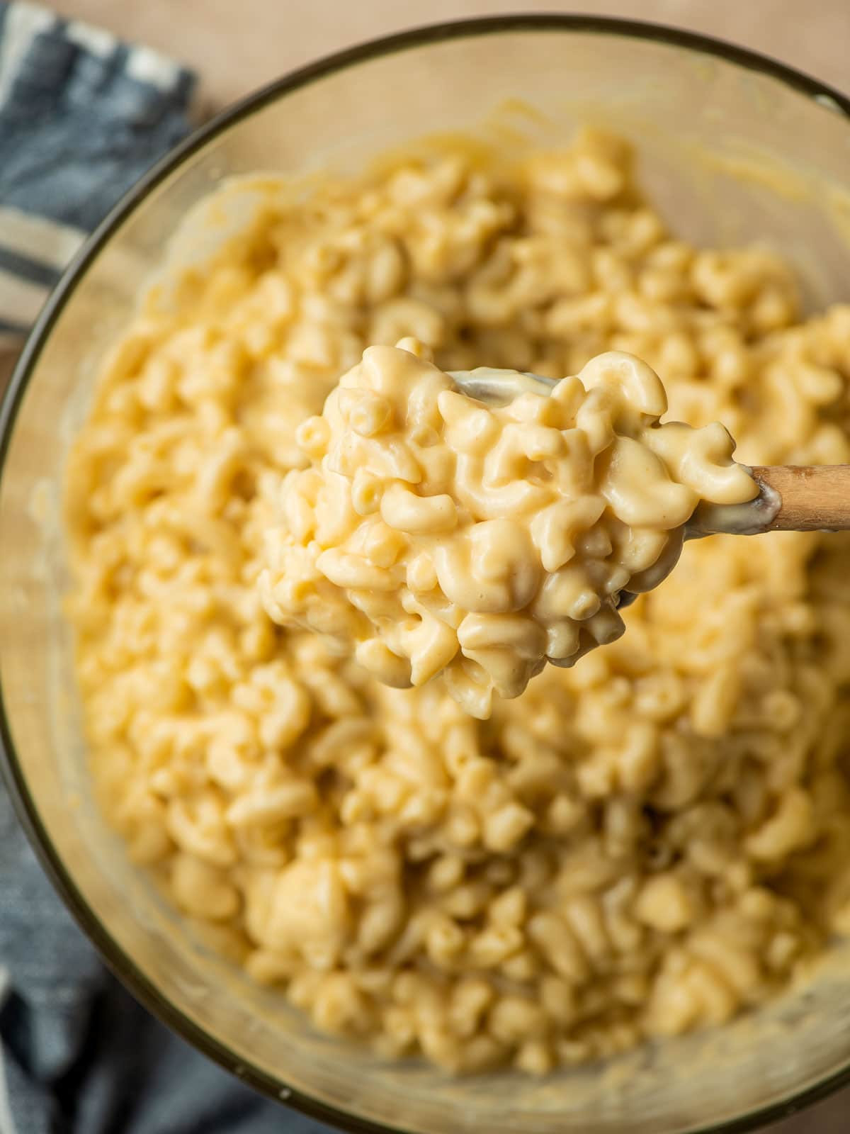 Wooden spoon scooping out creamy mac and cheese from a glass bowl.