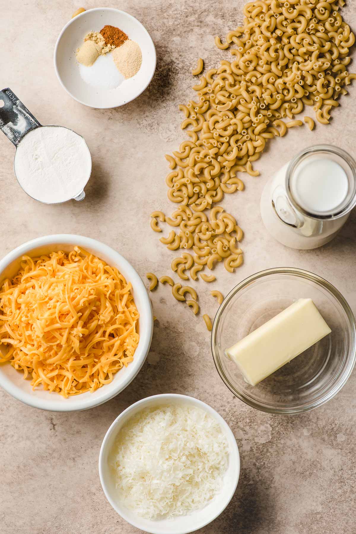 Ingredients for mac and cheese in prep bowls--butter, shredded cheese, flour, butter, pasta, and milk.