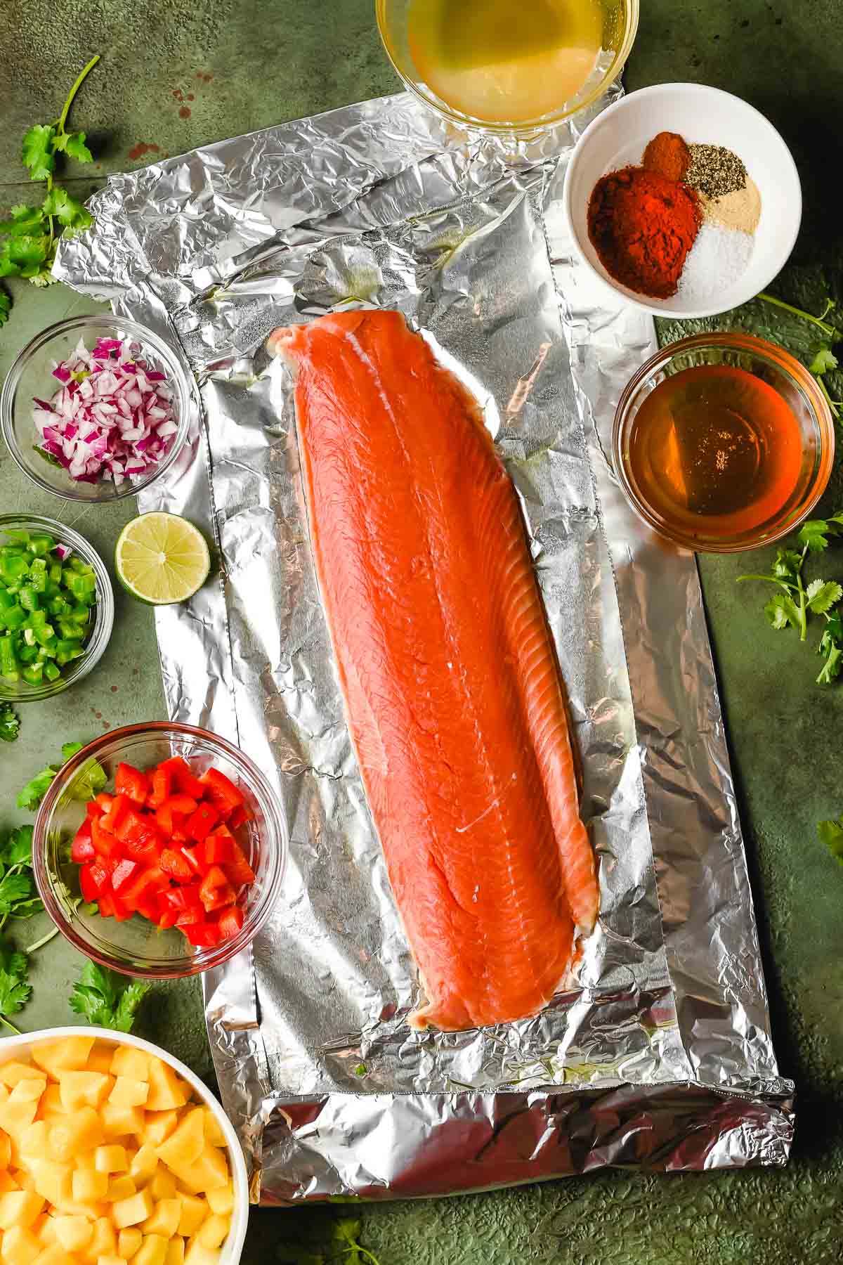 Raw salmon fillet shown on a large piece of foil, with other ingredients around it.