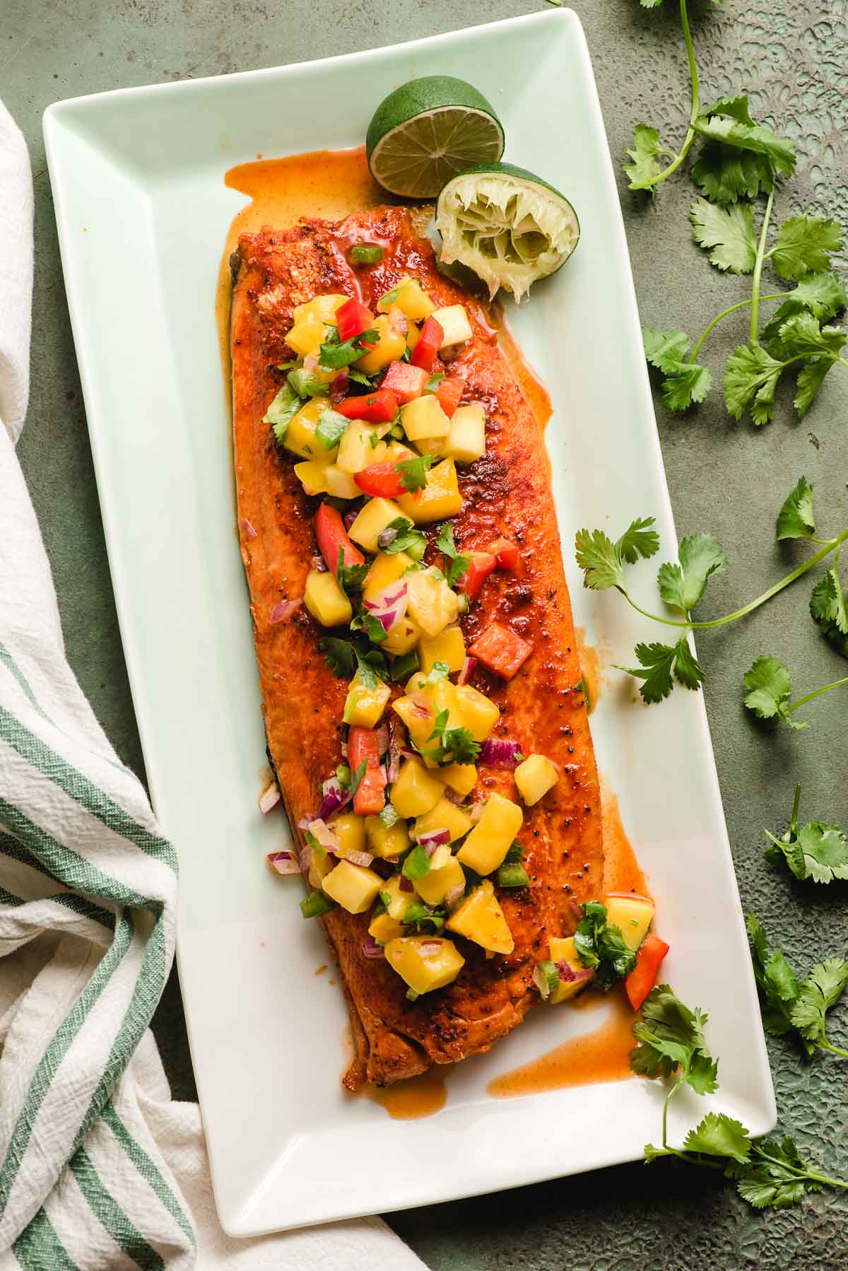 Grilled Salmon with Mango Salsa on top of a platter, and squeezed lime wedges on the side.