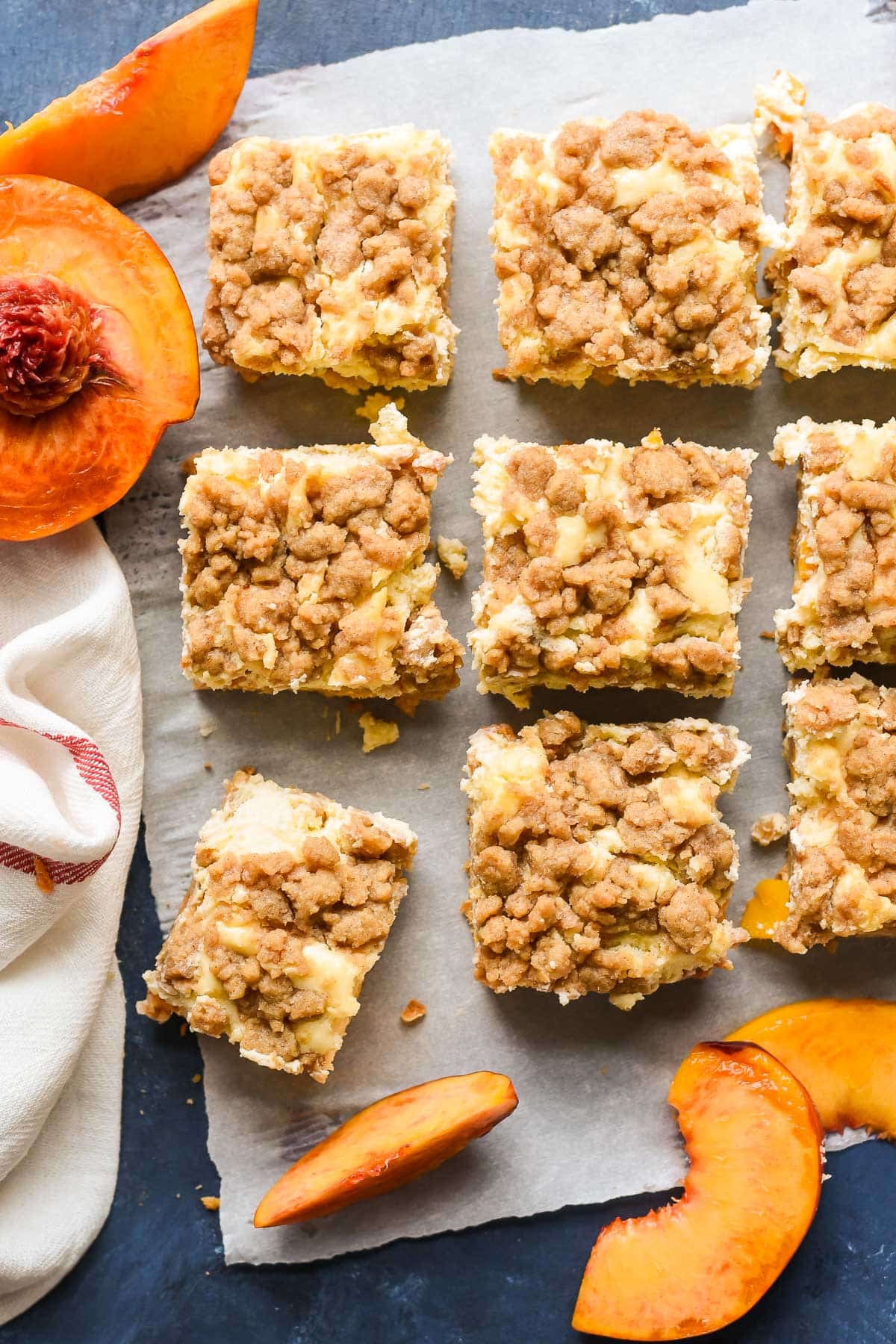 Sliced peach cheesecake bars surrounded by sliced peaches.