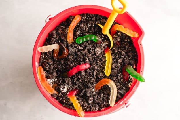 Red bucket filled with dirt pudding topped with gummy worms.
