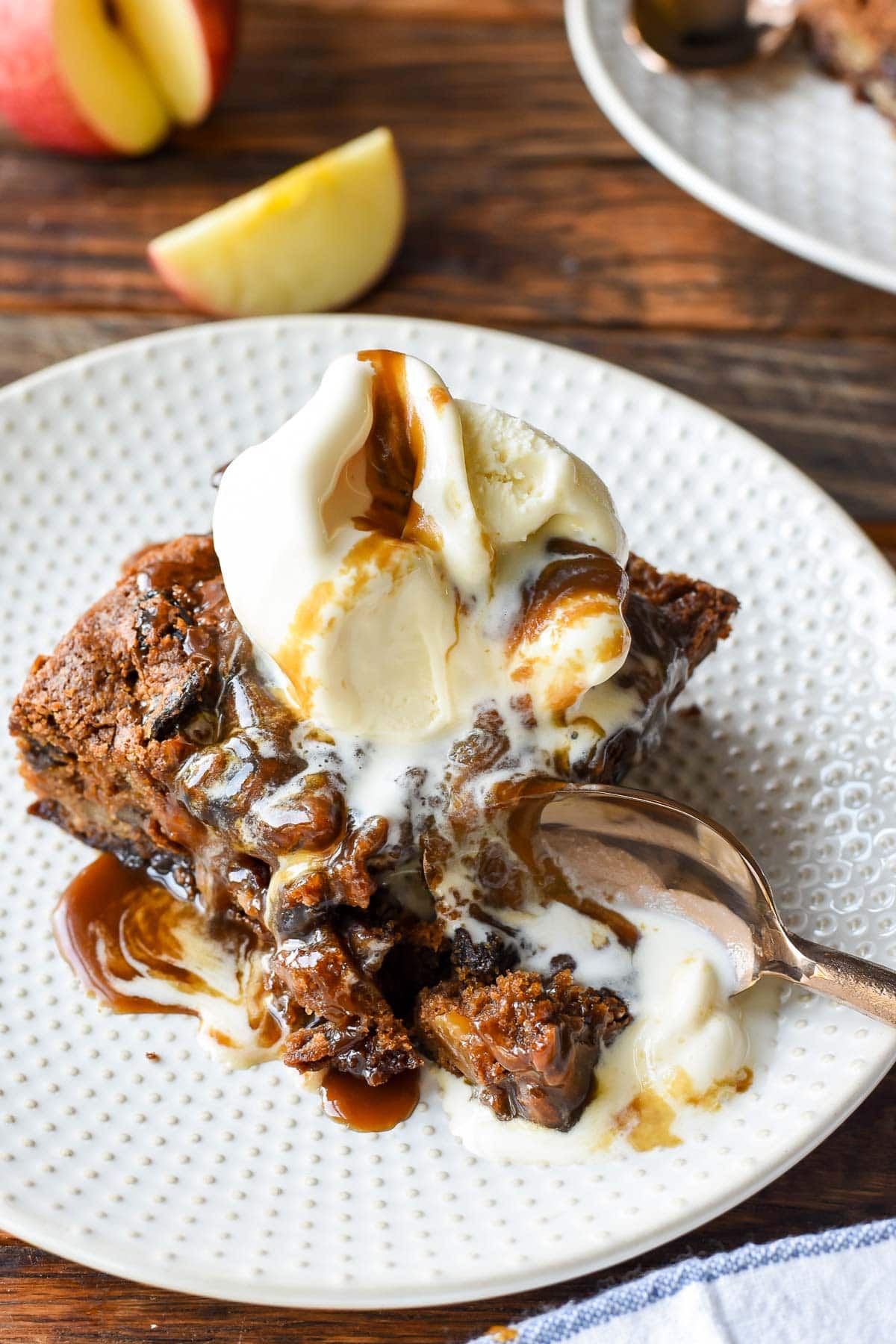 a spoon scoops a bite of of spiced apple cake, covered in ice cream and caramel sauce