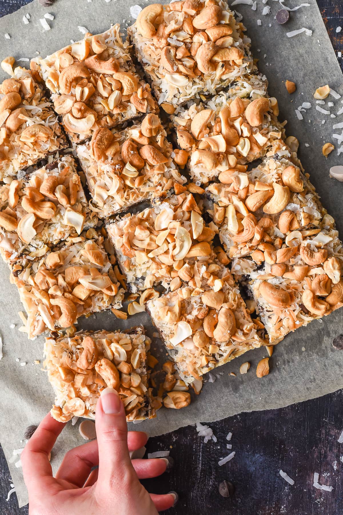 a hand takes a 7 layer bar from a group of them served on paper