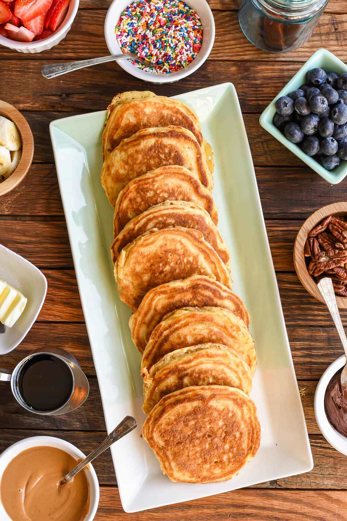 Large rectangular platter filled with fresh buttermilk pancakes with bowls of pancake toppings surrounding it.
