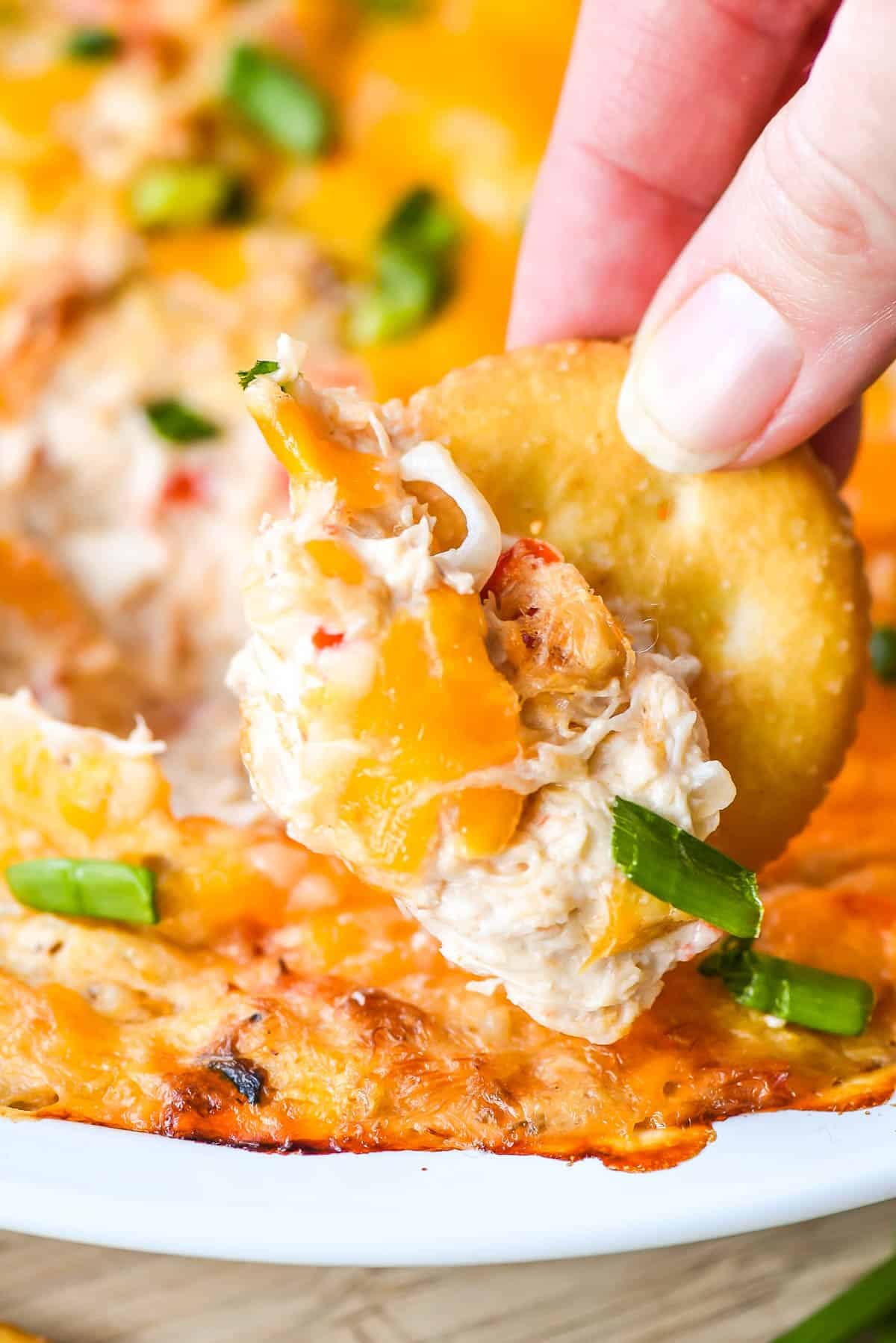 Hand dipping a Ritz cracker into warm crab dip.
