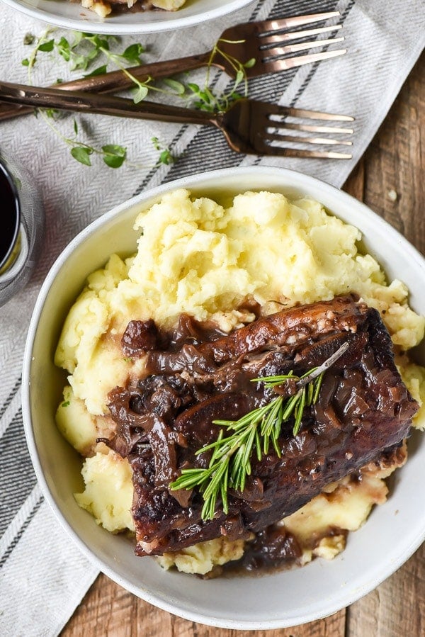 Red Wine Braised Short Ribs with mashed potatoes in a bowl with rosemary and thyme sprigs